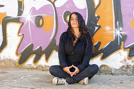 Young woman meditating at a graffiti brick wall