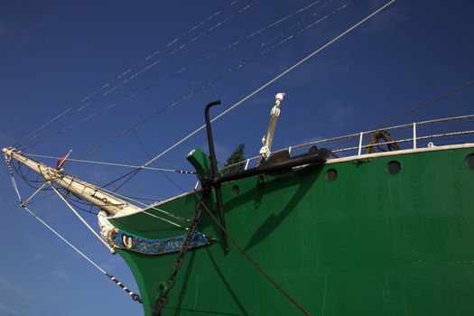 Low angle view of a bowsprit on a tall sailing ship with a green hull against a blue sky