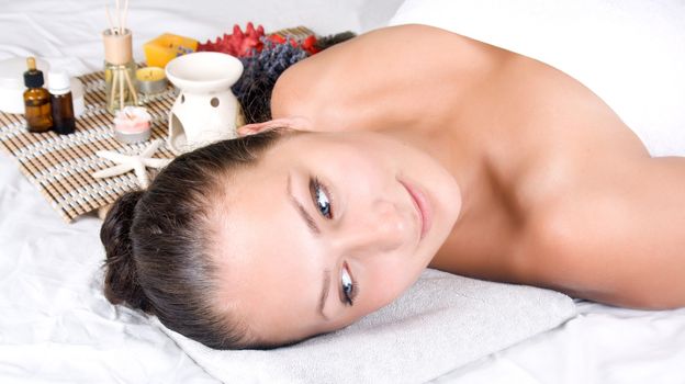 Woman on massage table with oils, essential oils, candles, scents. 