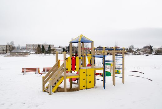 colorful playground on snowy frozen lake bank shore and living house district on other shore in winter.