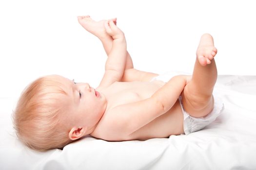 Cute adorable infant baby laying on back with feet up in the air wearing diapers, on white.