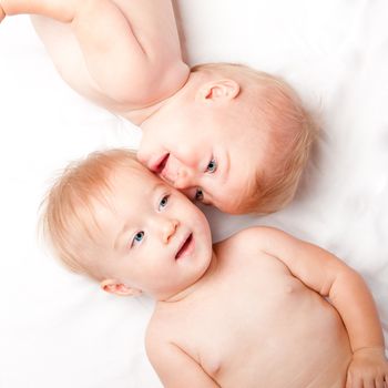 Two cute adorable twins faces showing special friendship connection while laying down, on white.