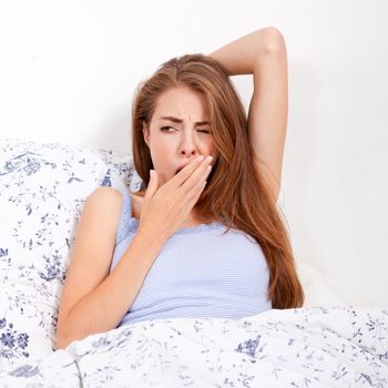 young attractive woman lying in bed yawing portrait tired in bedroom