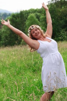 Young model with oversize stands with arms raised happily in a meadow in the high grass