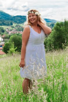 Young blond plus-size model in the white linen dress is laughing in a meadow with tall grass summer