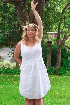 Young woman with fashionable white linen dress leaning against a tree