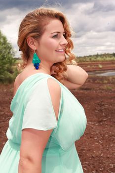 Blond young woman in an oversized aquamarine dress with matching earrings