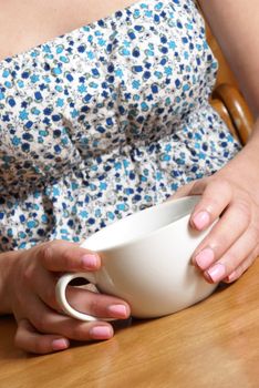 A woman holds her warm coffee cup in her hands at the cafe table.