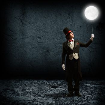 magician in top hat and tie, holding a glowing moon on a string