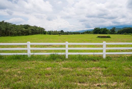 white fence in farm field and overcast sky