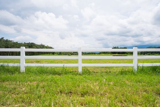 white fence in farm field and overcast sky