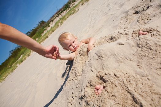 child in the sand with hand of parent