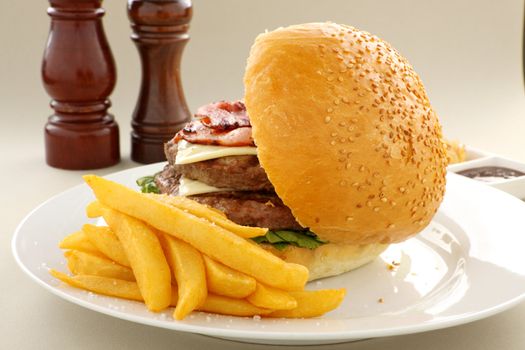 Fries on the side of a bacon and cheese buger with a sesame bun.