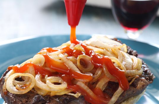 Tomato ketchup poured over fried onions on a steak burger.
