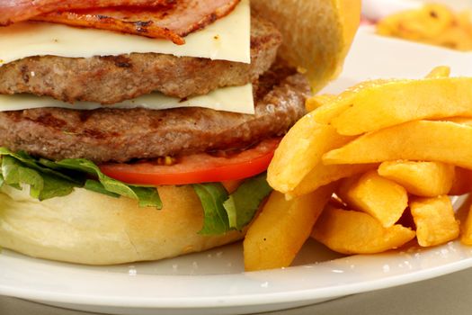 Double decker hamburger with bacon and cheese and golden fries.