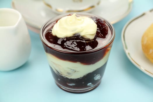 Strawberry jam topped with a dollop of cream in a glass ready to spread on scones.