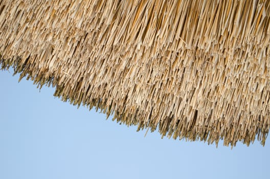 retro old natural organic construction straw house roof fragment on blue sky background.