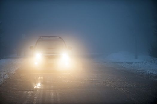 Bright headlights of a car driving on foggy winter road