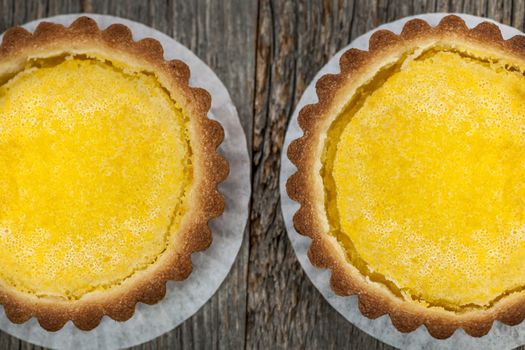 Two fresh gourmet lemon dessert tarts on wood background from above