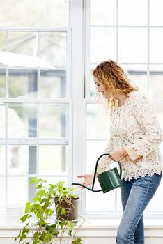 Smiling woman watering green plant at home by window