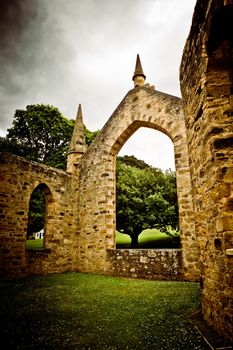 Beautiful arch framing a lovely green tree with spreading branches and topped with small turrets in an old stone building