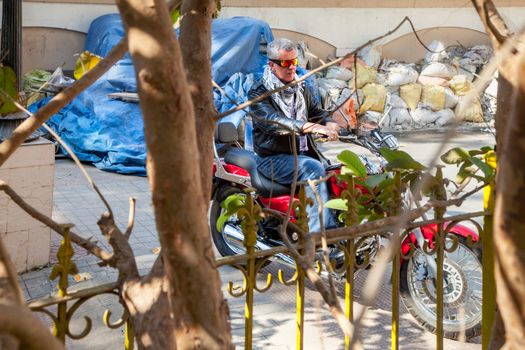 Horizontal color landscape capture of a senior caucasian male motorbike rider POV through trees and railings on a red cruiser wearing leather jacket in a relaxed pose.  Generic shot location Bombay India with model release