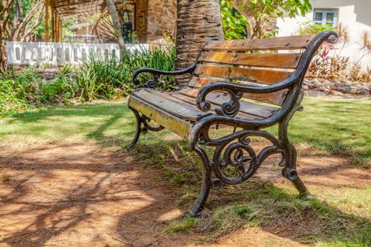 Horizontal color landscape of a wooden slat cast iron frame park bench in the shade of trees at a tropical garden. Shot location Bombay India