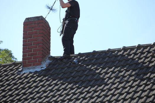Chimney sweep at work on the roof of a house busy inserting a chain and wire brush into the flue from above