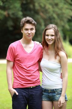 Young attractive teenage boy and girl standing arm in arm in a lush green park