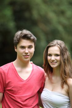 Portrait of a young teenage couple standing arm and arm against green foliage with copyspace