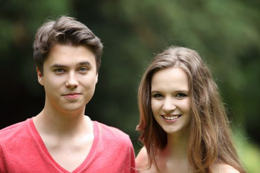 Smiling attractive young teenage boy and girl standing side by side in the sunshine in a green park