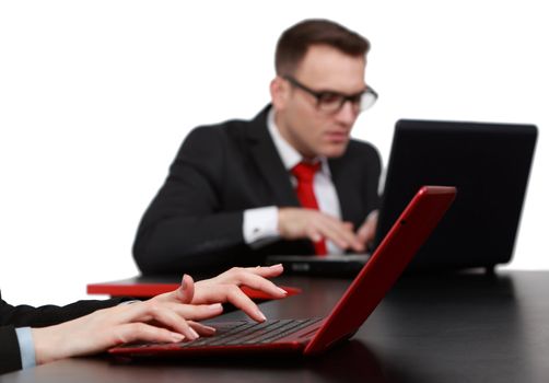 Close-up image of feminine hands working on a red notebook in front of a young woman using a laptop on a black table in an office.