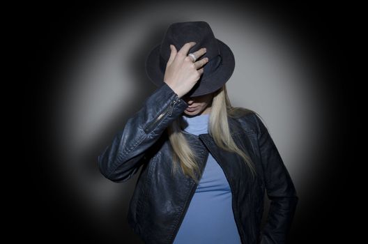 young blonde woman wearing a hat and a jacket on gray background under spotlight