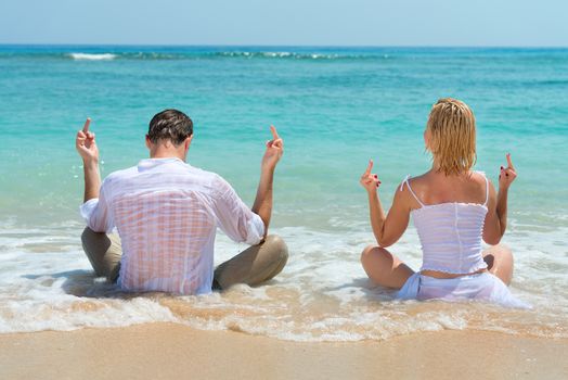 Happy young couple showing middle finger and enjoying at beach with blue sea on background