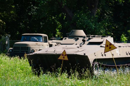 Abandoned military transport in green peace fields with radiation warning sign. 