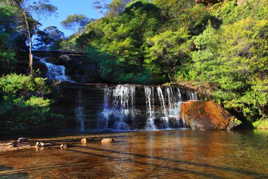 Just before the Jamison creek waters plunge over the sheer escarpment of the Blue Mountains, they fall in tiers known as Queens Cascades into a shallow sandy rockpool below, then flow over the sheer cliffs.