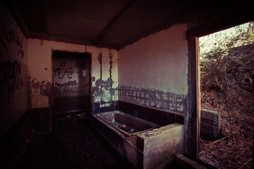 Dark atmospheric old bathroom in a abandoned dilapidated rural building with an opening to the exterior countryside