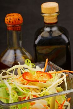 Close up of glass cup with salad, with vinegar and oil on the back