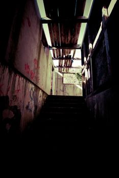 Dark interior stairs in a ramshackle dilapidated building with graffiti and missing roof timbers