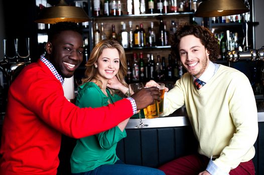 Three smiling young adult friends toasting with beer.