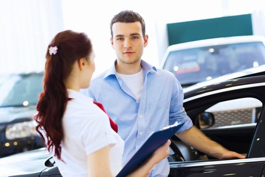 Young man choosing car at salon with help of consultant