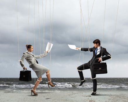 Image of businesspeople hanging on strings like marionettes against sea background. Conceptual photography