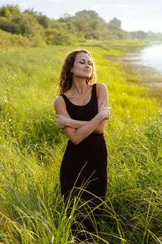 Beautiful girl walks and dreams in high grass on the banks of river