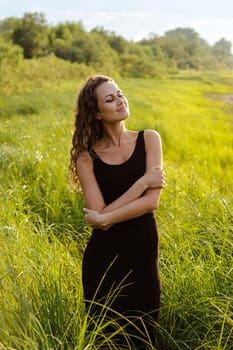 Beautiful girl walks and dreams in high grass on the banks of river