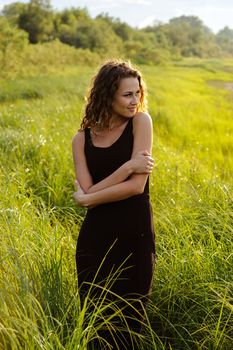 Beautiful girl walks and dreams in high grass on the banks of river