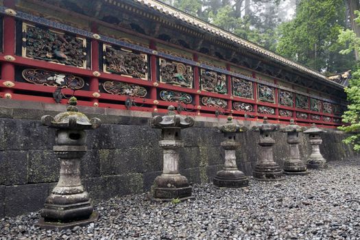 row of ancient stone lanterns close to red scenic wall of Japanese temple