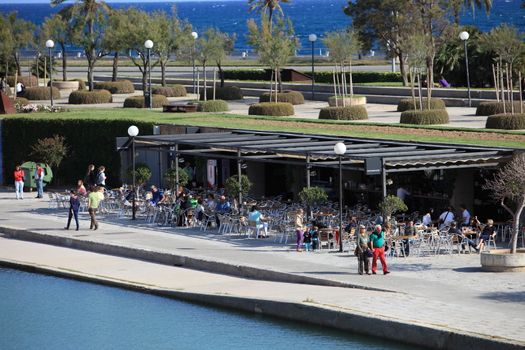 People seated at an open -air restaurant alongside water enjoying the hot tropical summer sun