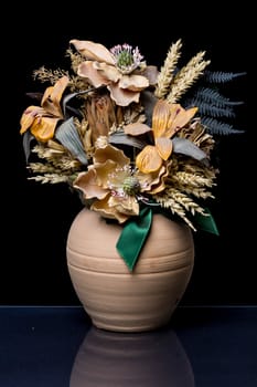 Flower composition in a Terracotta Vase with green ribbon on a reflective black surface with black background
