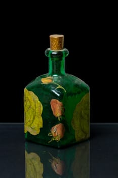 Decorated Decoupage green bottle on a reflective black surface with black background