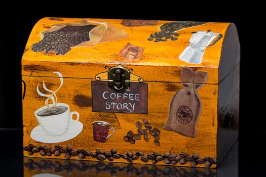 Decorative wooden box with coffee themed decoupage on a reflective black surface with black background